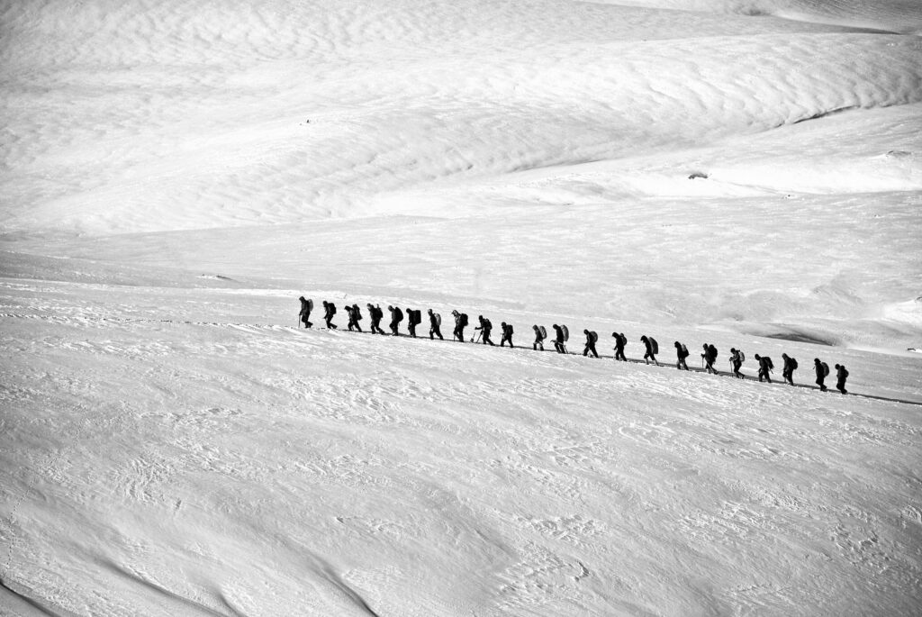 trekking-hiking-group-alpine-53214-53214 Silhouetted group hiking across a vast snowy landscape showcasing adventure and endurance.